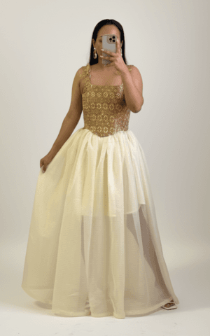 A high-end Ethiopian traditional dress, the Zewditu gown, featuring an intricate gold hand-woven bodice (Tilf) with a square neckline and a voluminous, multi-layered cream chiffon skirt against a professional studio background.